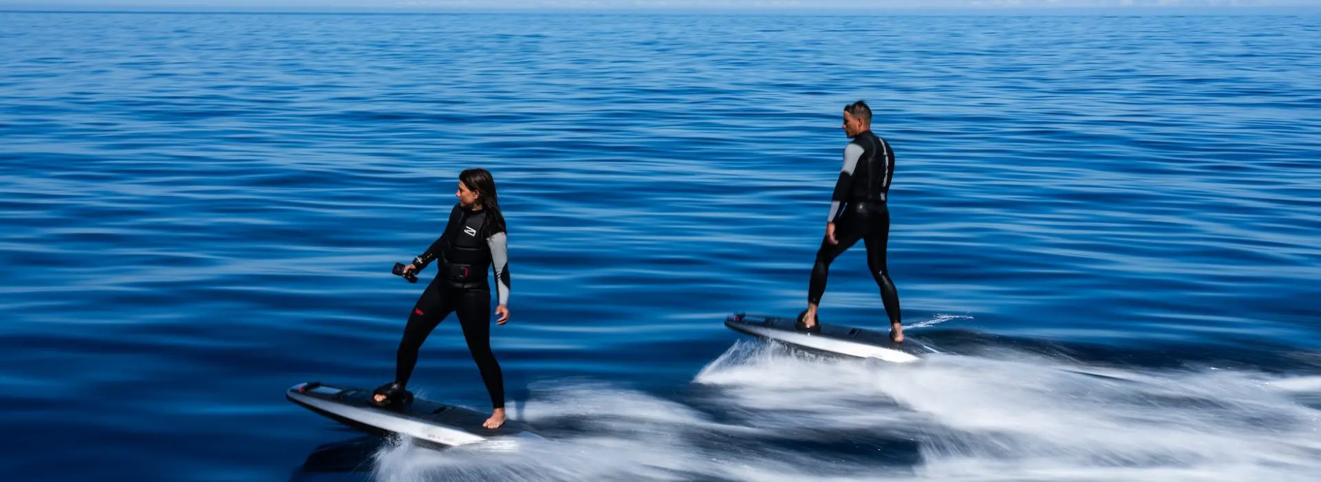 2 people riding Awake Boards in blue water.